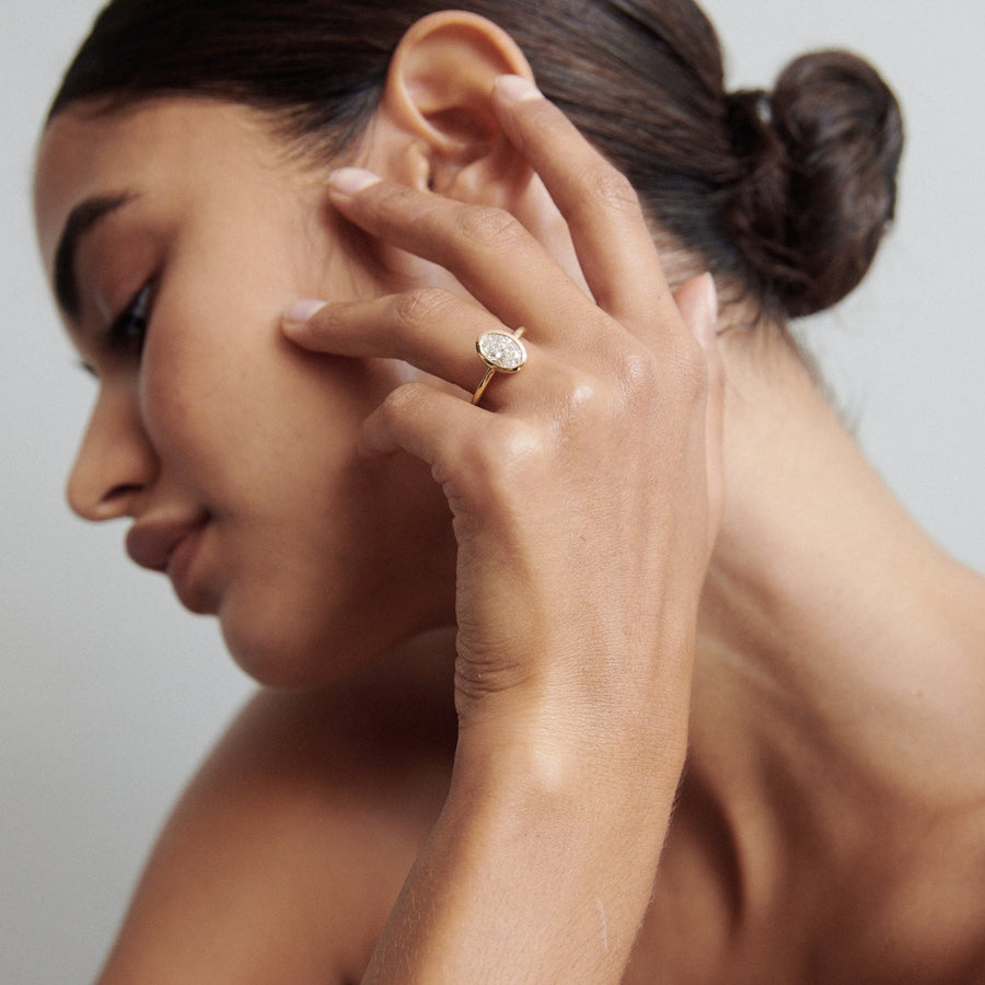 Oval cut lab grown diamond bezel engagement ring in polished gold band with secure modern setting