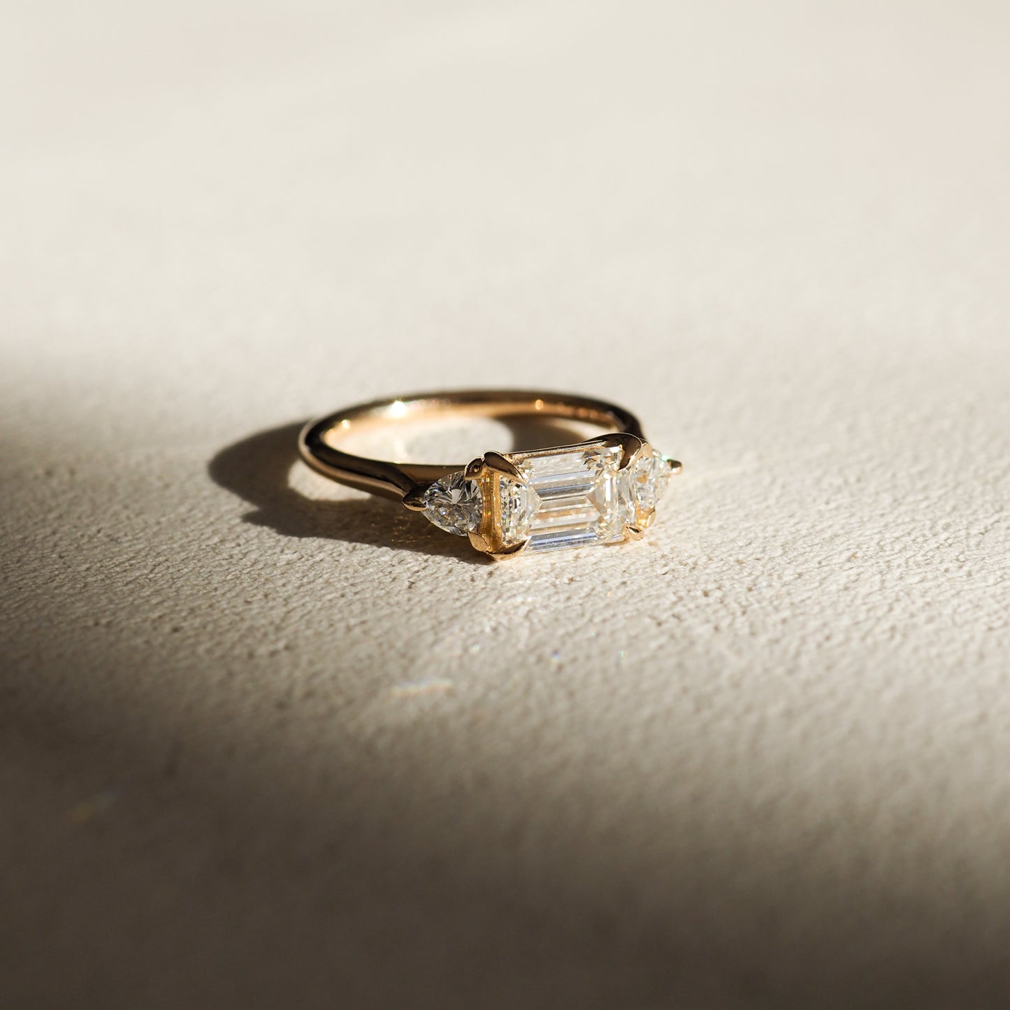 1.0 carat emerald cut lab grown diamond three stone engagement ring with side diamonds set on a polished gold band