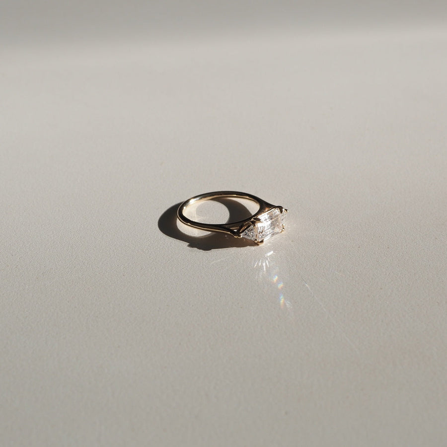 1.0 carat emerald cut lab grown diamond three stone engagement ring with side diamonds set on a polished gold band