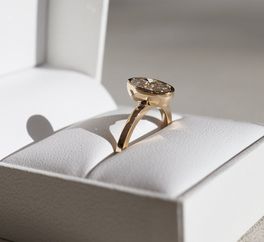 Oval cut lab grown diamond bezel engagement ring in polished gold band with secure modern setting