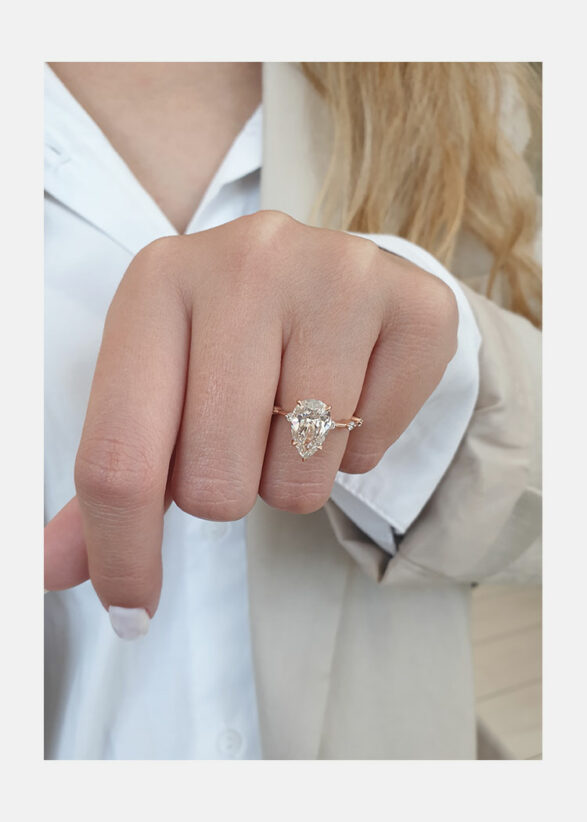Pear cut lab grown diamond dainty pavé engagement ring with delicate side stones set in a slim prong setting on polished gold band