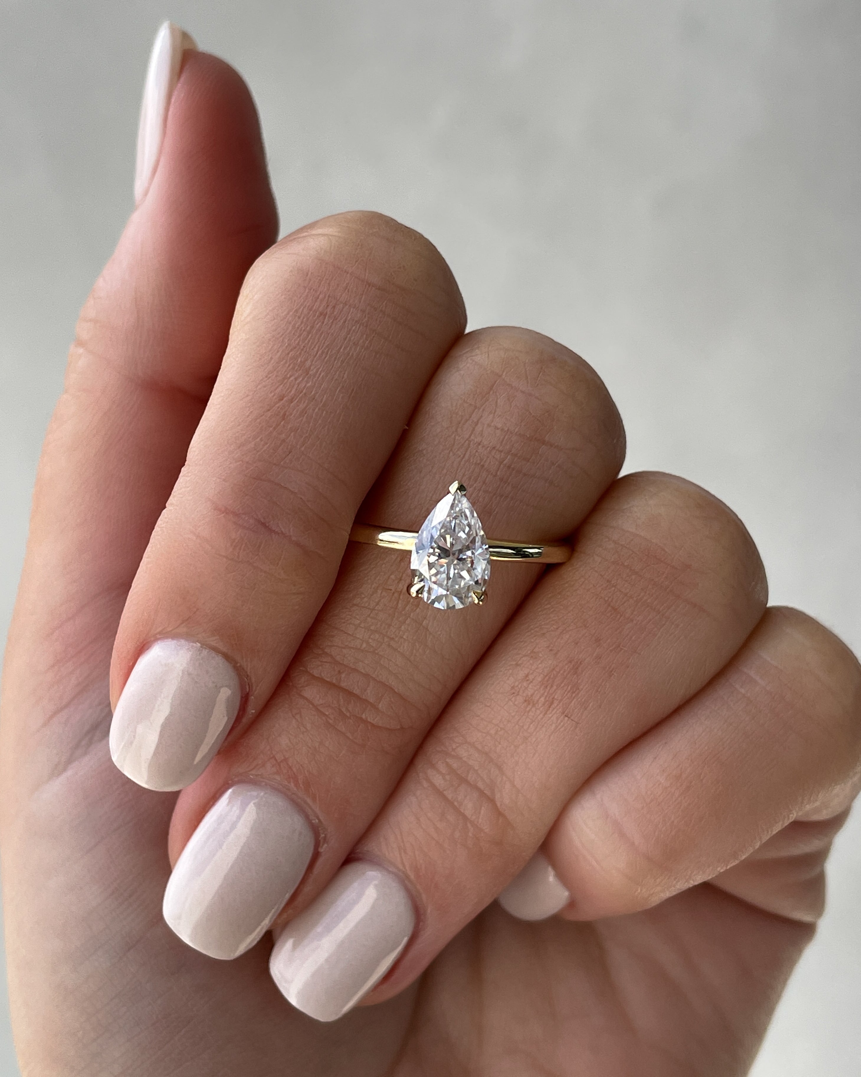 Pear cut lab grown diamond solitaire engagement ring in classic prong setting on polished gold band