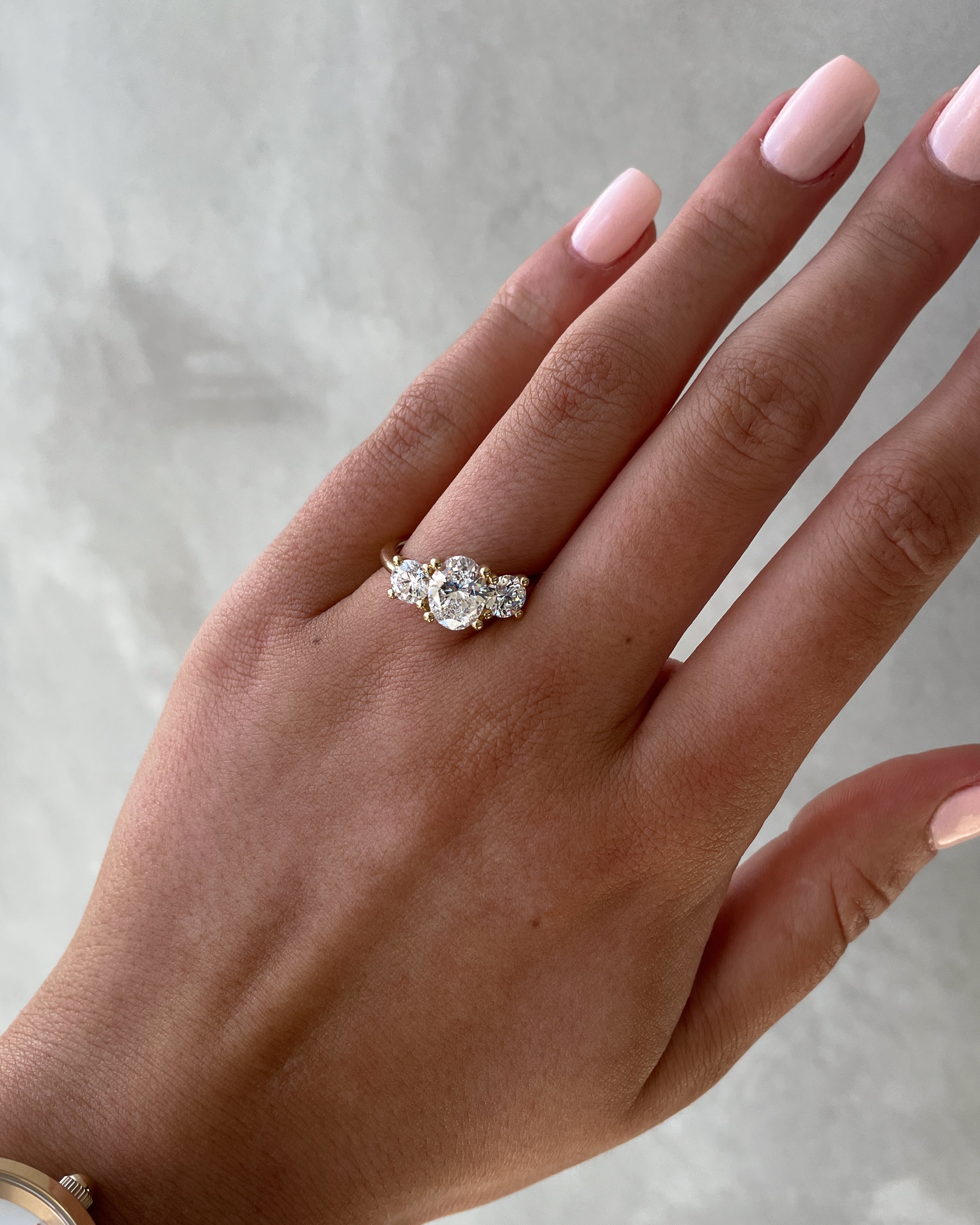 Oval cut lab grown diamond three stone engagement ring with center stone and side diamonds in classic prong setting on gold band