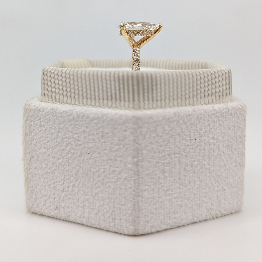 Pear cut lab grown diamond pavé engagement ring with side stones in prong setting on polished gold band