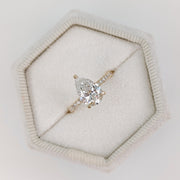 Pear cut lab grown diamond pavé engagement ring with side stones in prong setting on polished gold band