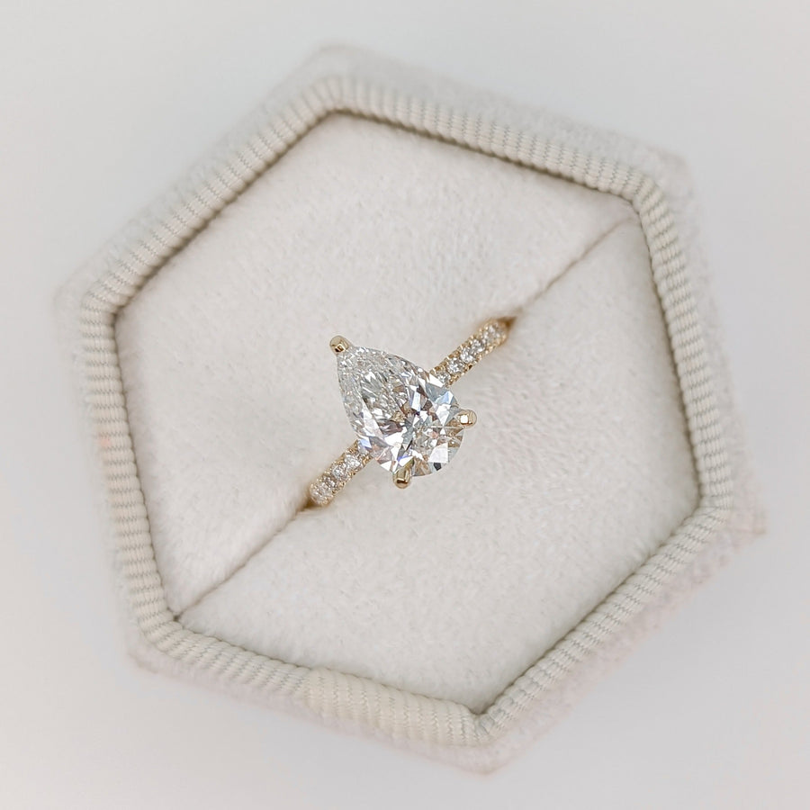 Pear cut lab grown diamond pavé engagement ring with side stones in prong setting on polished gold band