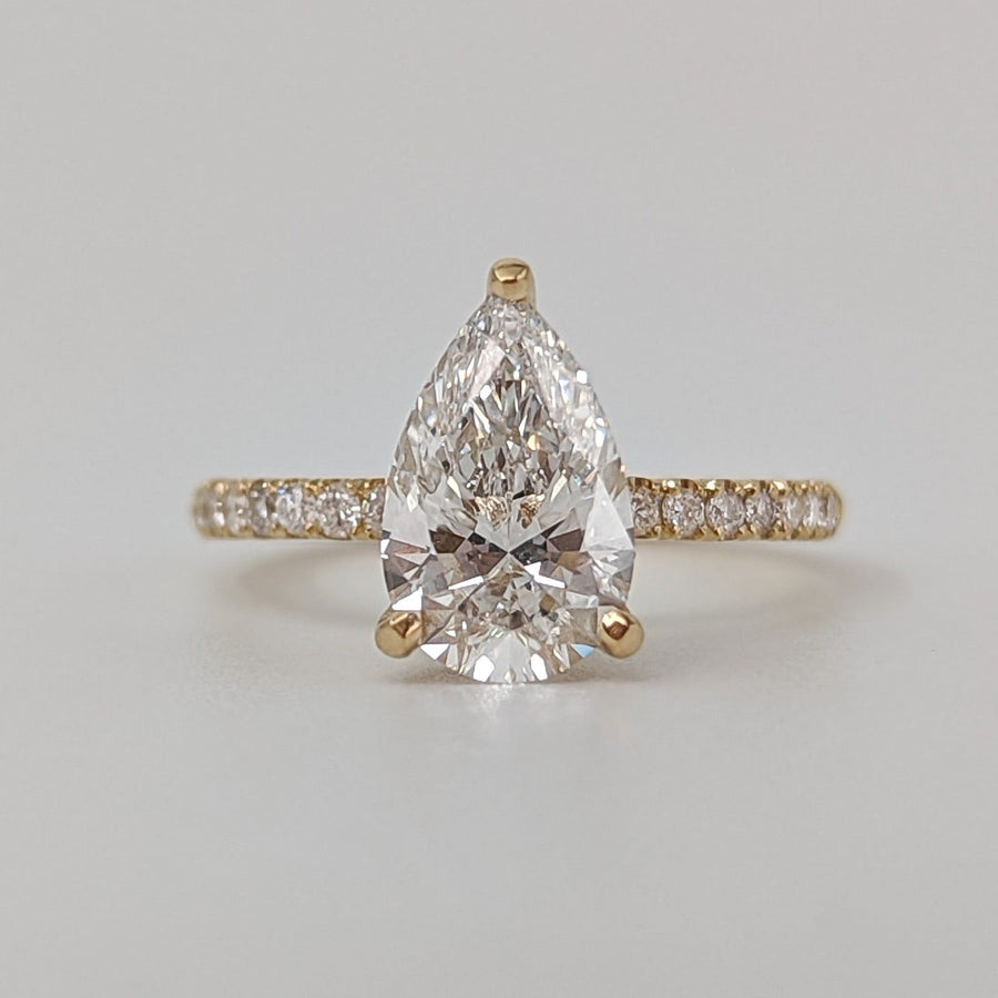 Pear cut lab grown diamond pavé engagement ring with side stones in prong setting on polished gold band