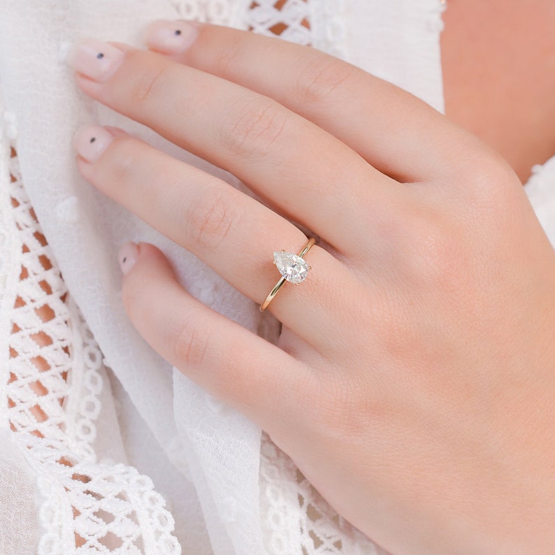 Pear cut lab grown diamond hidden halo engagement ring with sparkling accent stones set in polished gold band