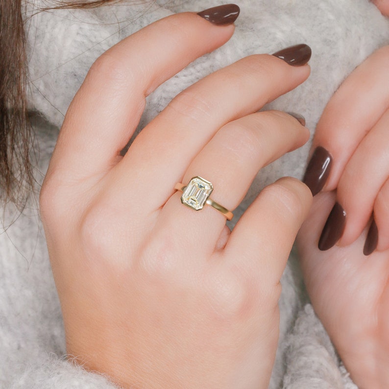 Emerald cut lab grown diamond bezel engagement ring set in sleek metal band with modern minimalist design