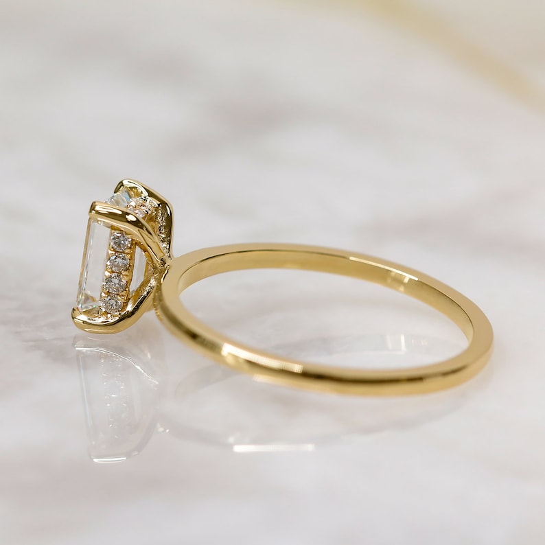 Emerald cut lab grown diamond hidden halo engagement ring with delicate prong setting and polished gold band