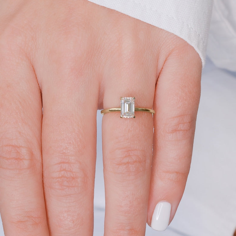 Emerald cut lab grown diamond hidden halo engagement ring with delicate prong setting and polished gold band