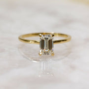 Emerald cut lab grown diamond hidden halo engagement ring with delicate prong setting and polished gold band