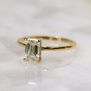 Emerald cut lab grown diamond hidden halo engagement ring with delicate prong setting and polished gold band
