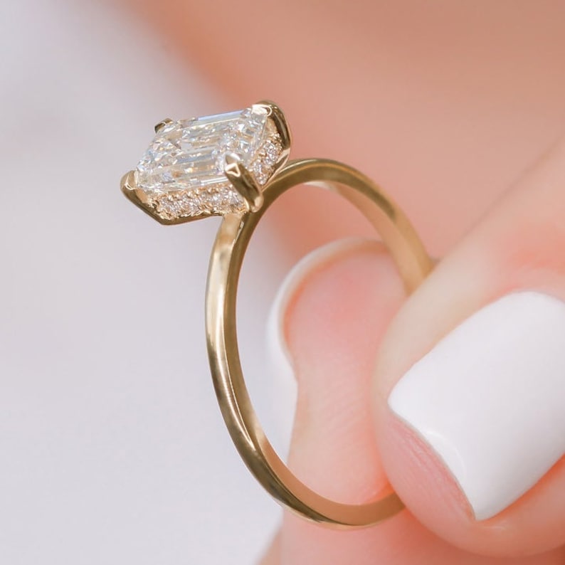 Emerald cut lab grown diamond hidden halo engagement ring with delicate prong setting and polished gold band