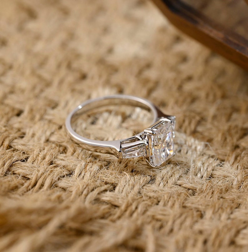 Radiant cut lab grown diamond three stone engagement ring with side stones in elegant prong setting on polished gold band