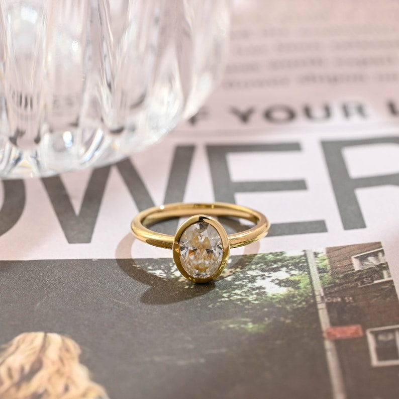 Oval cut lab grown diamond bezel setting engagement ring in polished gold band with modern minimalist design