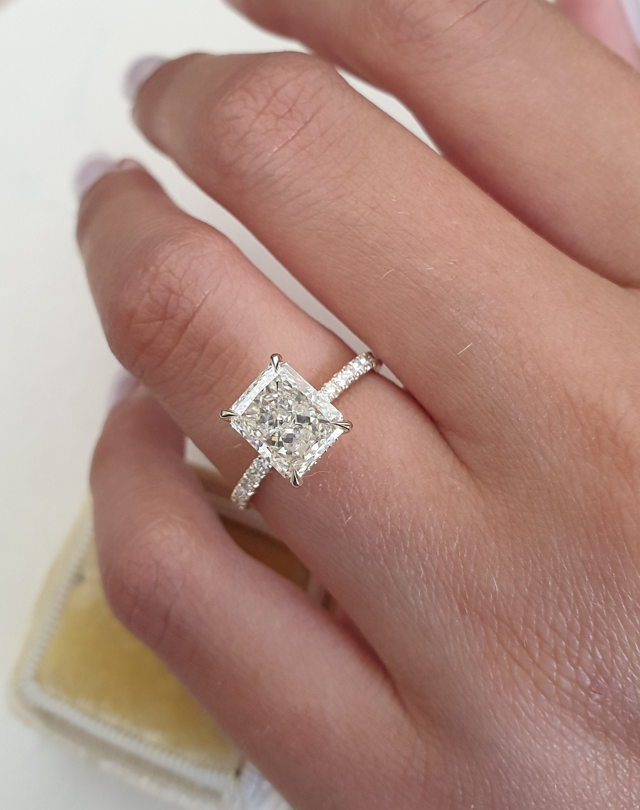 Radiant cut lab grown diamond pavé engagement ring with sparkling side stones set on polished gold band in prong setting