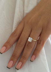 Radiant cut lab grown diamond engagement ring with hidden halo setting and prong design on polished gold band